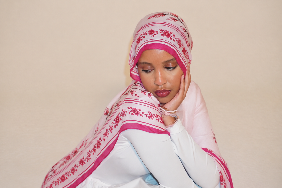 Rosy hijab with pale pink fabric, deeper pink floral sprigs and patterned borders, styled with a white top.